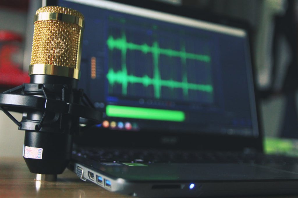 Close-up of a golden microphone and laptop used for audio editing.